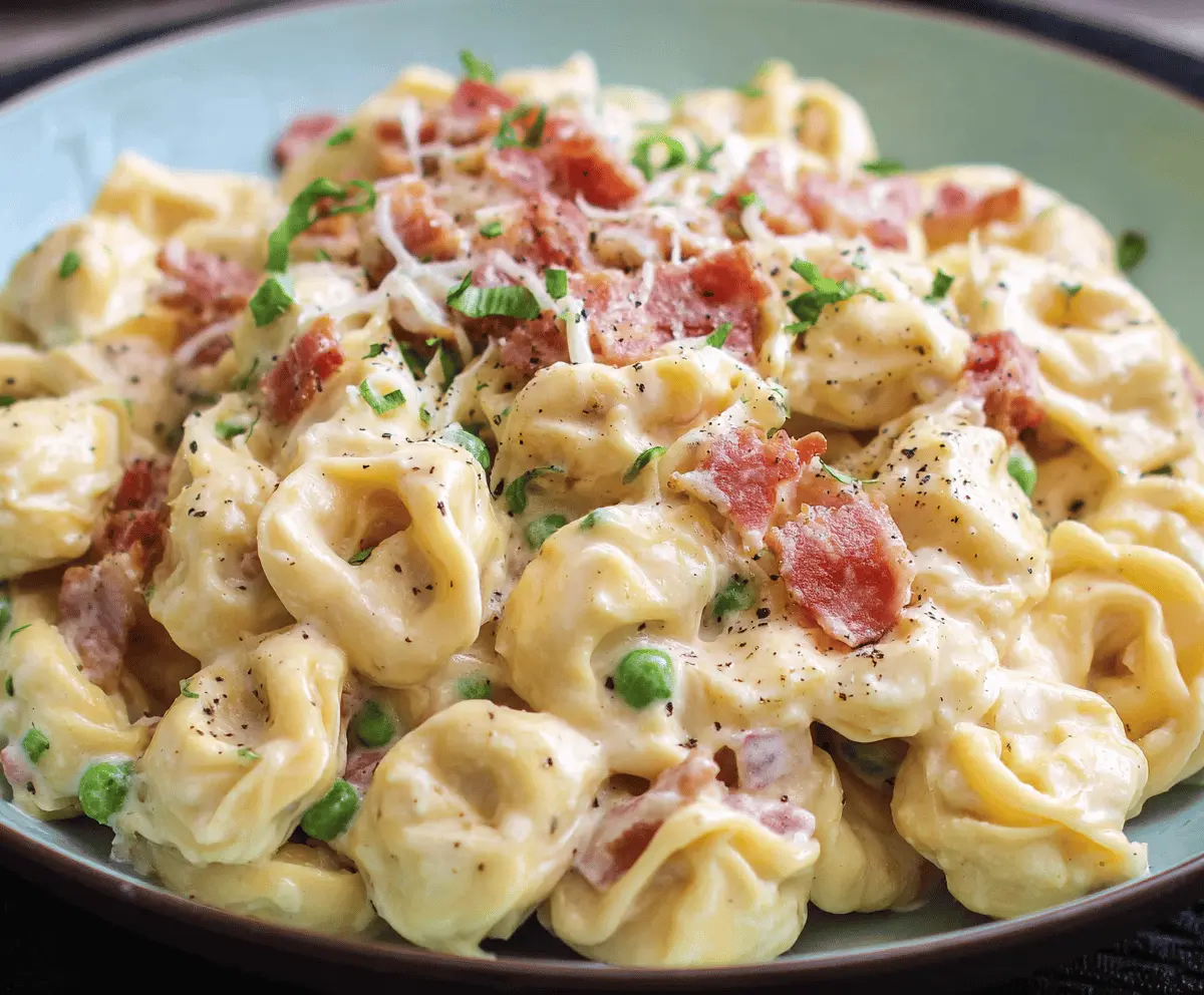 Creamy tortellini carbonara garnished with fresh herbs and grated Parmesan cheese in a white bowl on a wooden table