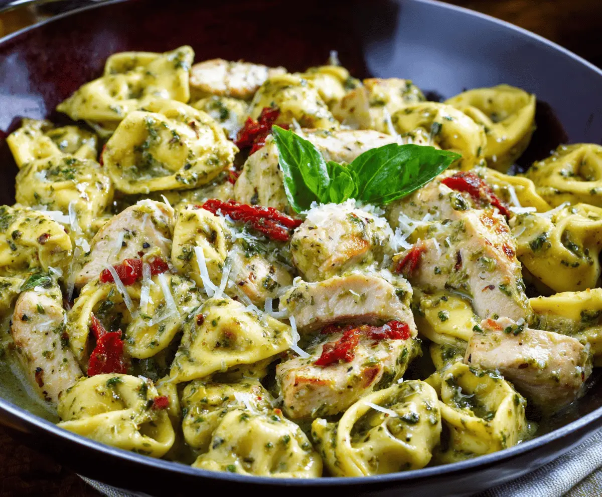 Delicious pesto chicken tortellini dish with fresh basil and melted cheese, served on a white plate