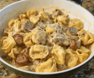 Creamy sausage and cheese tortellini alfredo dish with sliced sausage and fresh herbs on a white plate.