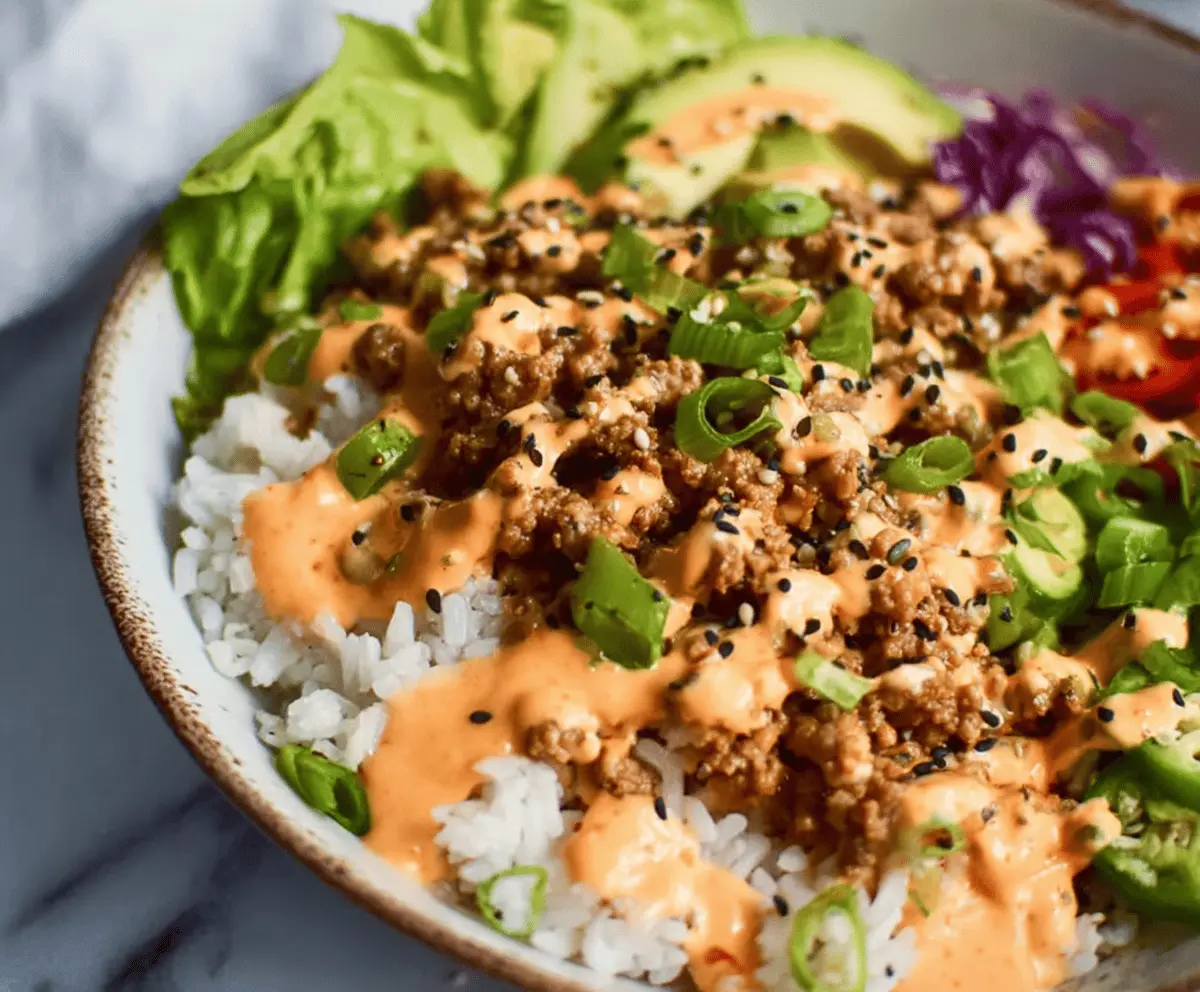 Ground turkey rice bowl topped with fresh vegetables and spicy Bang Bang sauce, served in a white ceramic dish.